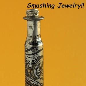 May include: A silver bullet casing with a gold paisley design, repurposed into a decorative piece of jewelry. The top of the casing has a silver ring attached to it.