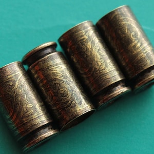 May include: Four gold-colored metal bullet casings with an intricate engraved design. The casings are arranged in a row, with the open ends facing the viewer.