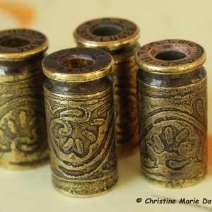 May include: Four gold-colored metal bullet casings with intricate engraved designs. Each casing has a different inscription on the top.