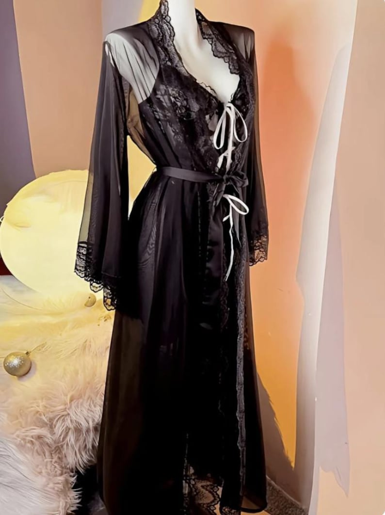 May include: A black sheer robe with lace trim and a matching lace slip. The robe has a satin sash and a V-neckline.