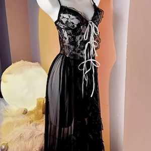 May include: A black lace lingerie dress with a white ribbon tie at the bust. The dress has a sheer skirt with a ruffled hem.