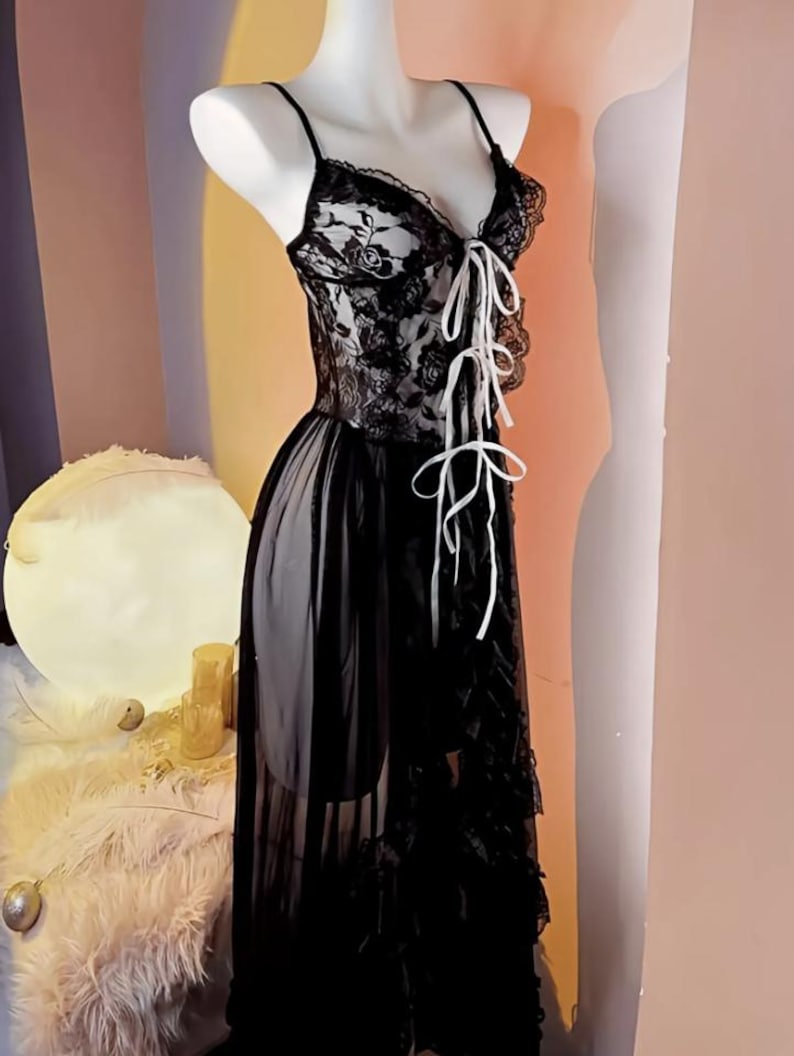 May include: A black lace lingerie dress with a white ribbon tie at the bust. The dress has a sheer skirt with a ruffled hem.
