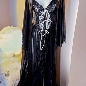 May include: A black sheer robe with lace detailing and a white satin ribbon tie. The robe has long sleeves and a flowing silhouette.