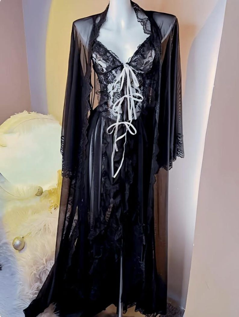 May include: A black sheer robe with lace detailing and a white satin ribbon tie. The robe has long sleeves and a flowing silhouette.