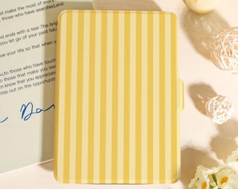 May include: A yellow and cream striped notebook cover with a tab on the right side. The notebook cover is rectangular and has vertical stripes. A handwritten note is partially visible in the background.