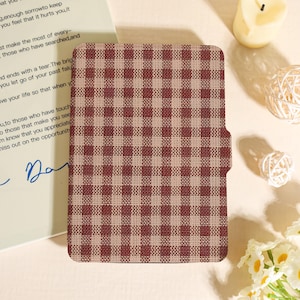 May include: A burgundy and beige checkered pattern cover, possibly for a notebook or tablet. The cover has a rectangular shape with rounded corners and a textured appearance. The design is a classic gingham style.