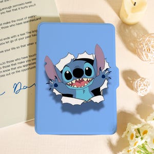 Può includere: Una custodia per tablet azzurra con un'immagine a cartoni animati di Stitch che sfonda un effetto carta strappata. Il personaggio è blu con grandi occhi, grandi orecchie e un ampio sorriso. La custodia ha una finitura liscia.