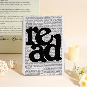 Puede incluir: Un objeto rectangular blanco con forma de libro con la palabra "read" en letras negras grandes. El fondo está lleno de texto pequeño. Una vela y bolas decorativas están en el fondo.