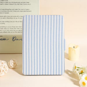 May include: A rectangular notebook with a light blue and white striped pattern. The notebook is closed and has a rounded edge. A candle and flowers are in the background.