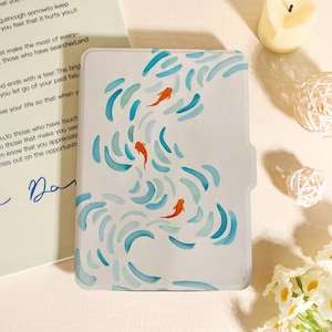 Könnte beinhalten: Weißes Etui mit einem Aquarelldesign von orangefarbenen Fischen, die in blauen und türkisfarbenen Wellen schwimmen. Das Etui hat eine gebogene Kante und einen seitlichen Ausschnitt. Das Design ist künstlerisch und skurril.