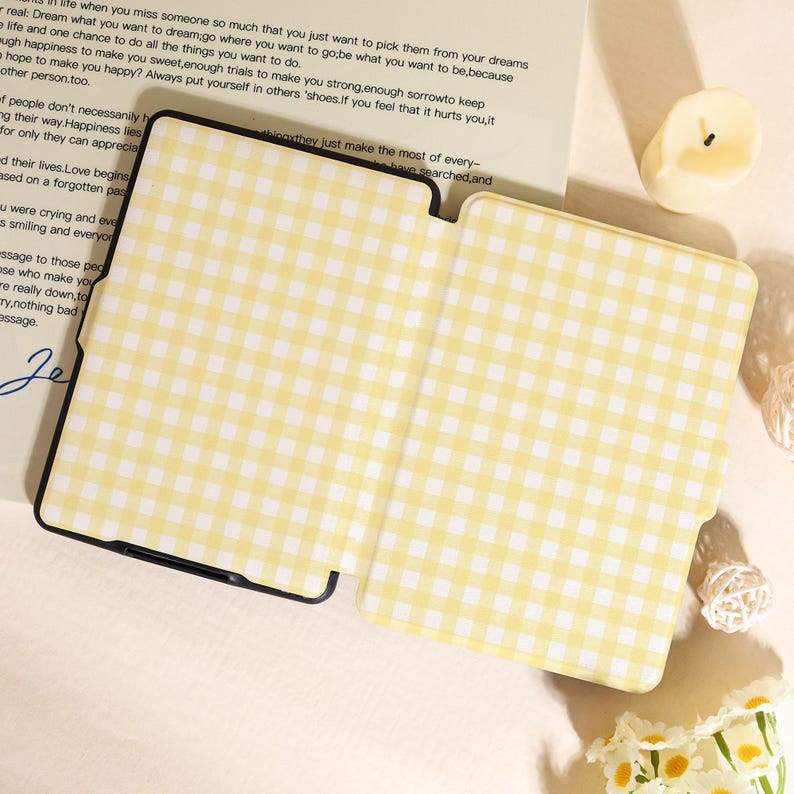 May include: A yellow and white gingham pattern tablet case, open and lying flat. The case has a black border and is on a light-colored surface. The case is next to a candle and a piece of paper with text.