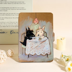 Peut inclure: Une couverture de carnet rectangulaire marron avec une illustration fantaisiste de deux chiens prenant le thé. L'œuvre d'art est dans des couleurs pastel douces, avec un abat-jour rose suspendu au-dessus. La couverture a un aspect texturé.