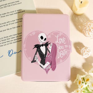 Puede incluir: Una funda rosa para tableta con Jack Skellington y Sally de Pesadilla antes de Navidad, dentro de un diseño floral en forma de corazón. También está presente el texto "Love You to Death". La funda es de color rosa liso.