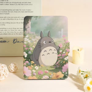 Peut inclure: Une housse de tablette avec un dessin animé de Totoro dans un champ de fleurs colorées. Le boîtier est gris et blanc avec une fermeture magnétique. L'arrière-plan représente une scène de forêt.