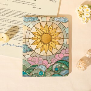 May include: A rectangular tablet case featuring a stained glass style illustration of a bright yellow sun centered above stylized pink clouds and swirling green and blue ocean waves, with dark outlines defining each geometric section.
