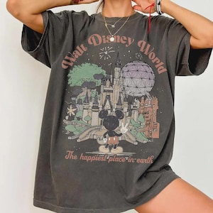 Puede incluir: Camiseta gris oscuro con un gr&aacute;fico colorido del castillo de Cenicienta, Spaceship Earth y Mickey Mouse. El texto dice "Walt Disney World" y "The happiest place in earth."