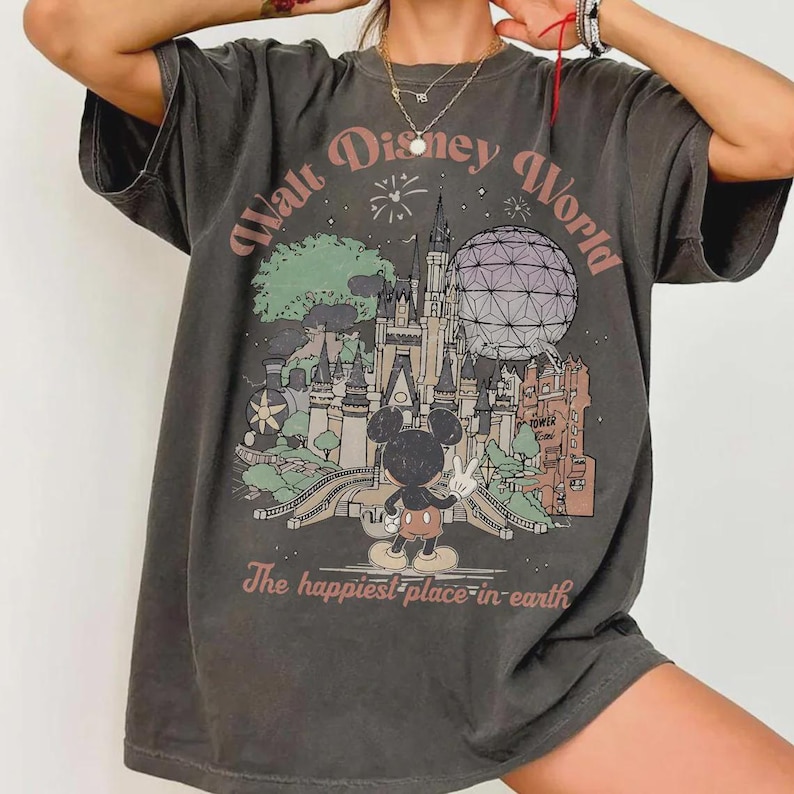 Puede incluir: Camiseta gris oscuro con un gr&aacute;fico colorido del castillo de Cenicienta, Spaceship Earth y Mickey Mouse. El texto dice "Walt Disney World" y "The happiest place in earth."