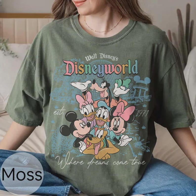 Op de afbeelding: Mosgroen T-shirt met een Disney World-afbeelding met Mickey Mouse, Minnie Mouse, Donald Duck, Daisy Duck, Goofy en Pluto. Het ontwerp bevat de tekst "Walt Disney's Disneyworld" en "Where dreams come true."