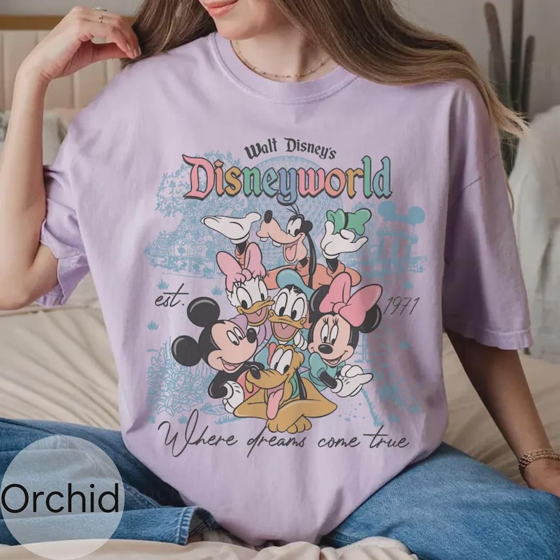 Op de afbeelding: Lichtpaars T-shirt met een Disney World-afbeelding met Mickey en Minnie Mouse, Donald en Daisy Duck en Goofy. Het shirt bevat de tekst "Walt Disney's Disneyworld" en "Where dreams come true."