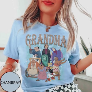 Puede incluir: Camiseta azul claro con la palabra "GRANDMA" en una fuente vintage. La camiseta presenta un gr&aacute;fico de varias abuelas animadas en varias poses. La camiseta est&aacute; hecha de un material suave.