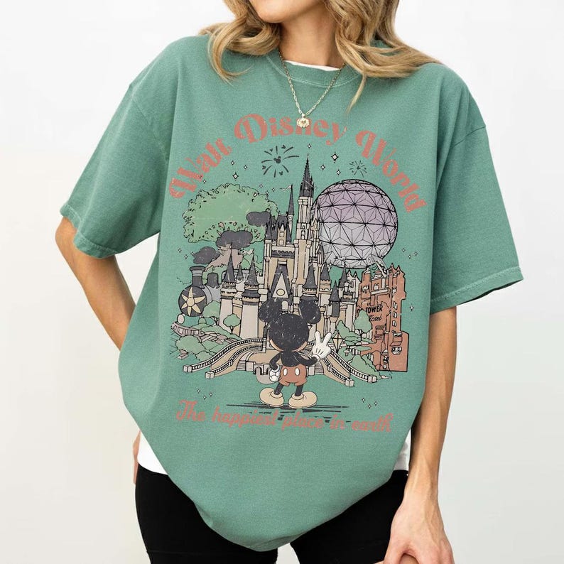 Puede incluir: Camiseta verde con un dibujo de Mickey Mouse frente a un castillo y una esfera geod&eacute;sica. El texto "Walt Disney World" y "The happiest place on earth" est&aacute;n impresos encima y debajo del dibujo, respectivamente.