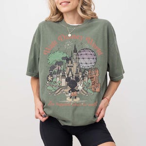 Puede incluir: Camiseta verde oliva con un gr&aacute;fico retro de Walt Disney World. El dise&ntilde;o incluye el castillo de Cenicienta, Spaceship Earth y Mickey Mouse. El texto dice "Walt Disney World" y "The happiest place on earth."