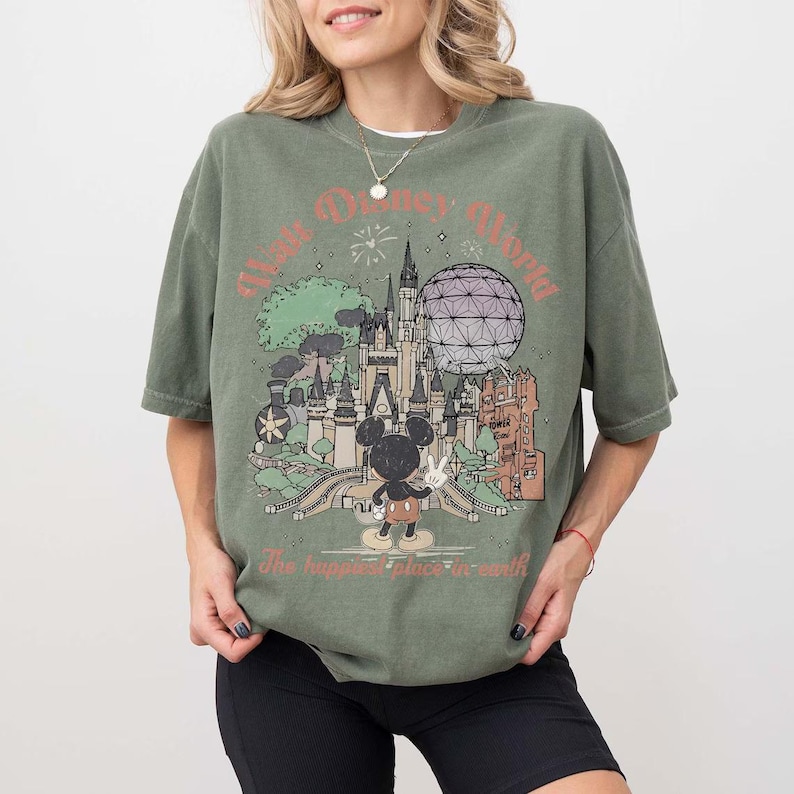 Puede incluir: Camiseta verde oliva con un gr&aacute;fico retro de Walt Disney World. El dise&ntilde;o incluye el castillo de Cenicienta, Spaceship Earth y Mickey Mouse. El texto dice "Walt Disney World" y "The happiest place on earth."