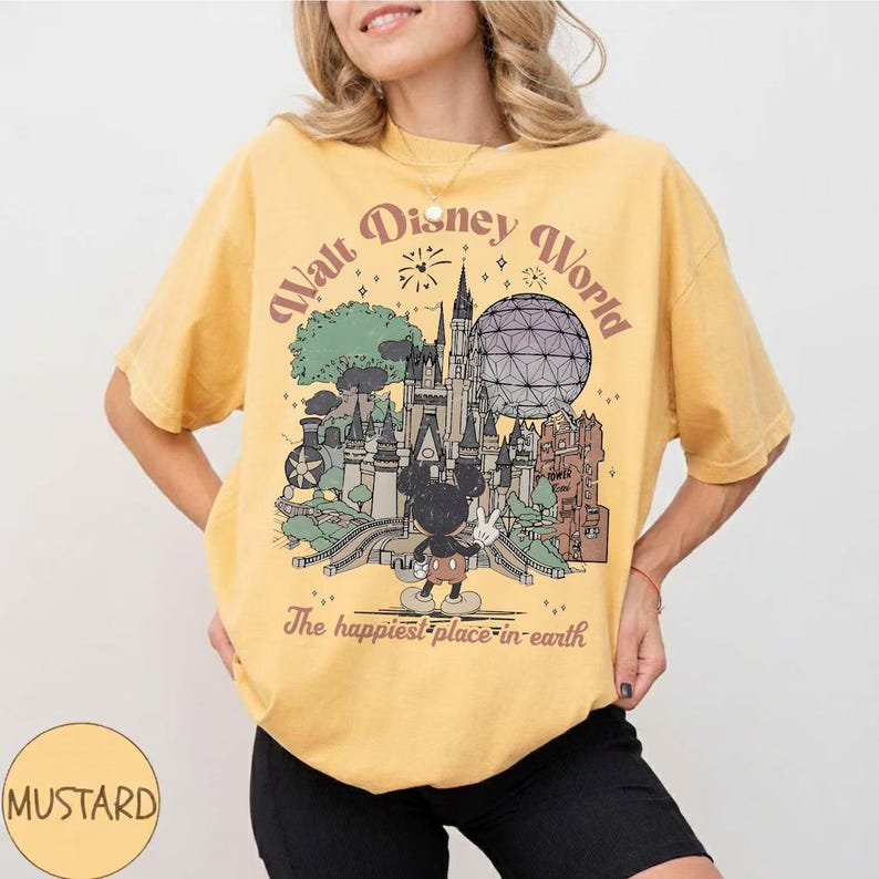 Puede incluir: Camiseta amarilla mostaza con un gr&aacute;fico de Walt Disney World con Mickey Mouse, un castillo y Spaceship Earth. El texto dice "The happiest place on earth."