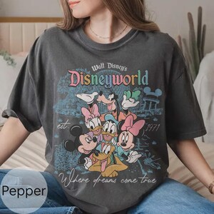 Op de afbeelding: Donkergrijs t-shirt met een kleurrijk Disney World-ontwerp met Mickey Mouse, Minnie Mouse, Donald Duck, Goofy en Pluto. De tekst bevat "Walt Disney's Disneyworld", "est. 1971" en "Where dreams come true".