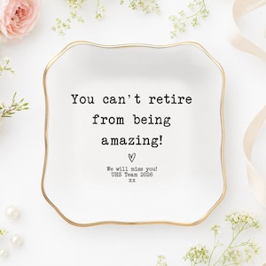May include: A square white ceramic trinket dish with scalloped edges and a gold-colored rim. The center features black text that reads: You can't retire from being amazing! followed by a heart symbol and the text: We will miss you! UHS Team 2026 xx.