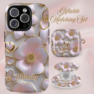 May include: A phone case, an earbud case, and a phone grip featuring a 3D-style pink and white floral pattern with gold outlines and heart accents. The phone case displays the name Mandy in gold script. The text Giftable Matching Set is visible.