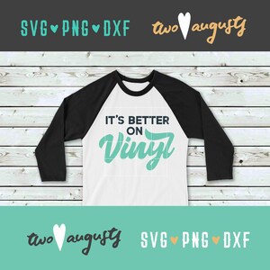 May include: A white and black baseball style shirt with the text "It's Better On Vinyl" in teal lettering. The shirt is on a wood background.