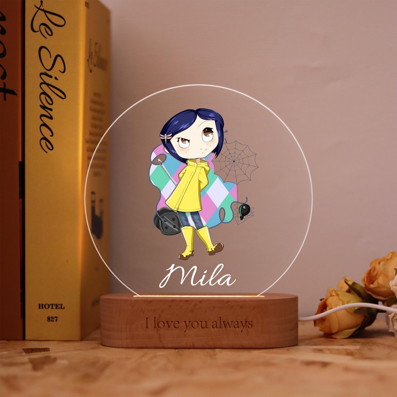 May include: A decorative night light featuring a cartoon character in a yellow raincoat, blue pants, and yellow boots. The character is standing in front of a colorful design with a spider web. The base is wooden and has the text "I love you always".