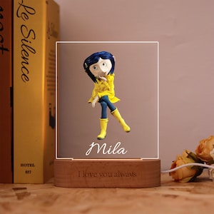 May include: A decorative night light featuring a cartoon character in a yellow raincoat and boots, with blue pants. The name "Mila" is written on the light, and the base reads "I love you always."