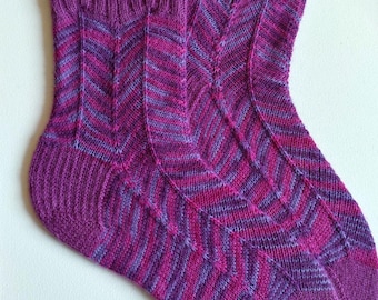 May include: A pair of purple and pink striped knitted socks. The socks have a chevron pattern and are made with a soft yarn.