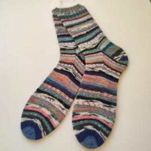 May include: A pair of knitted socks with a striped pattern. The socks display a mix of colours, including blue, pink, orange, and grey, in horizontal stripes. The toes and cuffs are solid blue and grey. The socks are made of a knitted material.