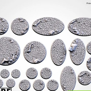 Può includere: Una collezione di basi in miniatura grigie e strutturate in varie forme: rotonde, ovali e oblunghe. Le basi presentano un motivo di terra screpolata con piccoli dettagli di rocce e detriti.