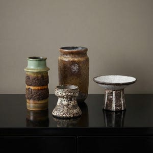 Può includere: Una collezione di quattro vasi in ceramica che include un vaso alto testurizzato verde e marrone, un grande vaso cilindrico screziato marrone, un piccolo contenitore a forma di ciotola color crema e marrone e un'ampia ciotola con piedistallo bianco e marrone.