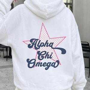 May include: A white hooded sweatshirt featuring a large pink star graphic on the back with a polka dot pattern. The text Alpha Chi Omega is printed in a dark blue cursive font across the center of the star. The hoodie has long sleeves and a hood.