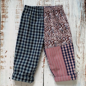 May include: Patchwork trousers with a mix of patterns. One leg is navy and white gingham, the other is a combination of floral, pink striped, and navy and pink gingham fabrics. The trousers are cuffed at the ankles.