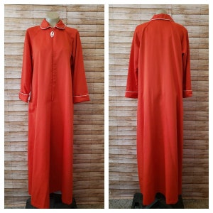 May include: A long, red robe with white piping around the collar, cuffs, and pockets. The robe has a zipper closure and a decorative button at the neckline.