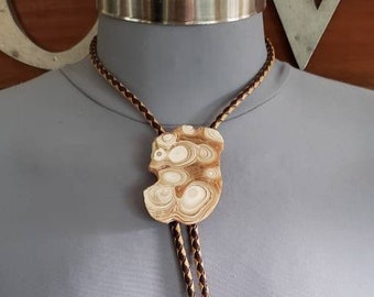May include: A brown and tan leather bolo tie with a large, white and brown agate stone pendant.