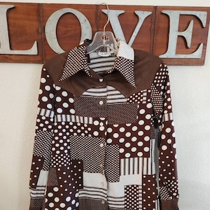 May include: A brown and white long-sleeved button-up shirt with a patchwork design. The shirt has a collar and a button closure. The fabric is a blend of cotton and polyester.
