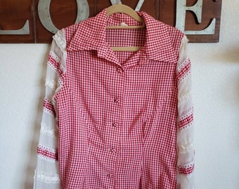 May include: A red and white gingham button-up shirt with sheer white lace sleeves. The shirt is hanging on a wooden hanger. The shirt has a classic collar and buttons down the front.