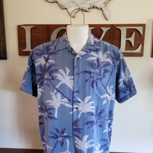 May include: A blue short-sleeved button-down shirt with a white palm tree print.