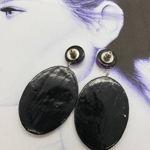 May include: A pair of black oval-shaped earrings with a purple and silver accent. The earrings are dangling and have a silver post.