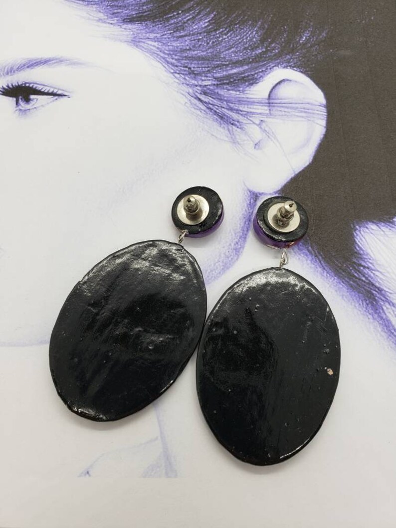 May include: A pair of black oval-shaped earrings with a purple and silver accent. The earrings are dangling and have a silver post.