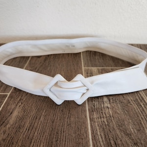 May include: A white ceramic mug with a black handle and the text "But First, Coffee" in a bold, black font. The mug is set against a blurred background, highlighting its clean design.