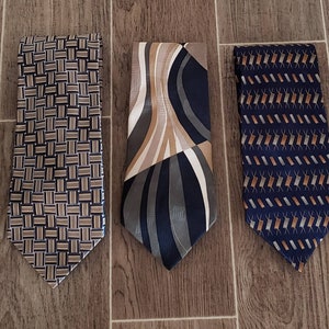 May include: Three silk neckties with different patterns. The first tie has a brown and beige woven pattern. The second tie has a blue, brown, and beige abstract pattern. The third tie has a blue and brown geometric pattern.
