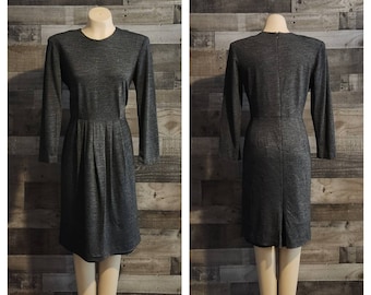May include: A gray, long-sleeved dress with a round neckline and pleated skirt. The dress is displayed on a mannequin, showcasing the front and back views. The fabric has a subtle textured pattern.